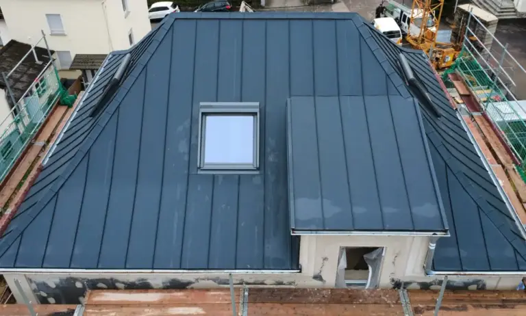 Ein Foto eines anthrazitfarbenen Daches mit Dachgaube und Dachfenster von schräg oben.